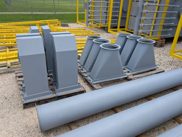 Primed gray duct transition fittings and round pipe sections staged on pallets outside